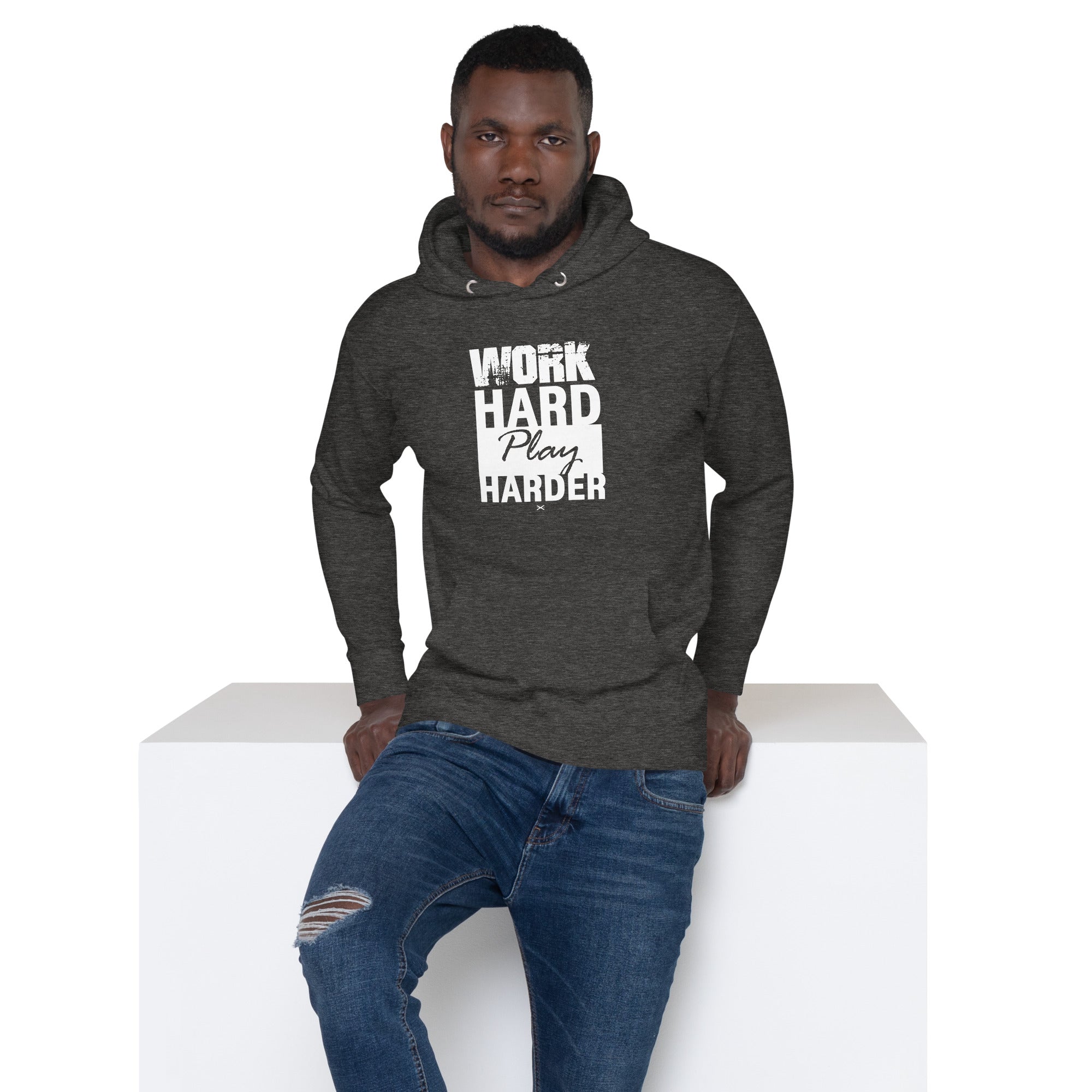 Man wearing a dark gray hoodie with 'Work Hard Play Harder' text, sitting on a white box.